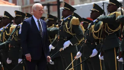 EPA Joe Biden reviews a guard of honour as he arrives at the presidential palace in Luanda. He is walking past a group of soldiers in formal uniforms, wearing white gloves and holding swords.