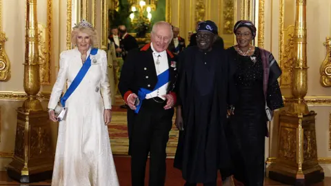 PA Media Britain's Queen Camilla in a floorlength cream dress, King Charles III in a black suit jacket and trousers and white waistcoat, Nigeria's President Bola Tinubu in a navy blue outfit and Nigeria's First Lady Oluremi Tinubuin an all-black ensemble